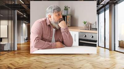 Portrait of sad senior man sitting at table in kitchen Wall mural