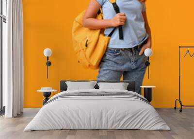 Portrait of teenage girl with backpack and headphones on yellow background Wall mural