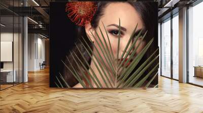 Portrait of young woman with beautiful professional makeup and palm leaf on dark background Wall mural