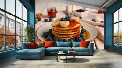 Pouring honey onto tasty pancakes with banana and blueberry on light wooden background, closeup Wall mural