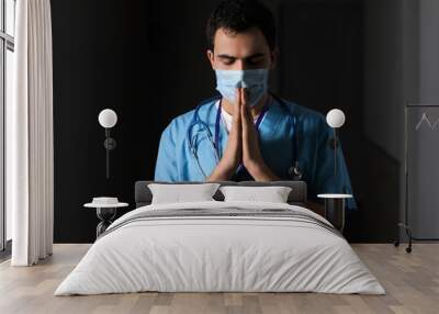 Praying male doctor on dark background Wall mural