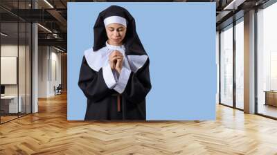 Praying young nun on blue background Wall mural