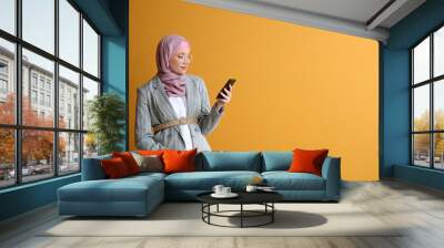 Pregnant Muslim woman using mobile phone on color background Wall mural