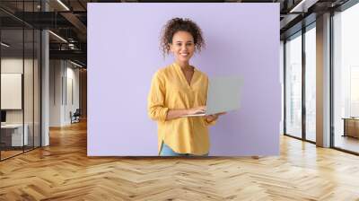 Pretty African-American woman using laptop on lilac background Wall mural