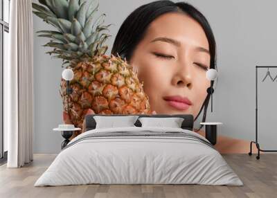 Pretty young Asian woman with pineapple on grey background Wall mural