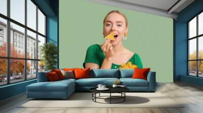 Pretty young woman eating nachos on green background Wall mural