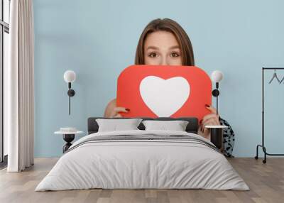 Pretty young woman holding heart like icon on blue background Wall mural