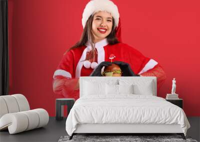 Pretty young woman in Santa costume with tasty burger on red background Wall mural