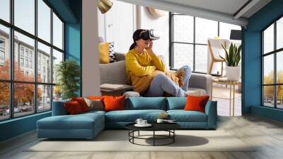 Pretty young woman in VR glasses sitting in sofa at home Wall mural