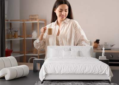 Pretty young woman with cup of hot coffee and newspaper at home Wall mural