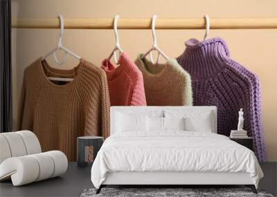 Rack with sweaters near beige wall, closeup Wall mural