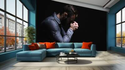 Religious young man praying to God on black background Wall mural