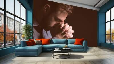 Religious young man praying to God on black background Wall mural