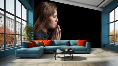 Religious young woman praying to God on dark background Wall mural