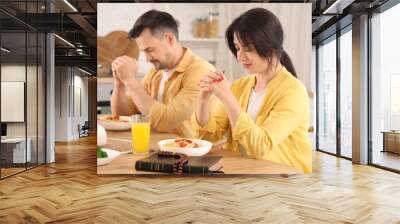 Religious young woman with her husband praying before dinner at table in kitchen Wall mural