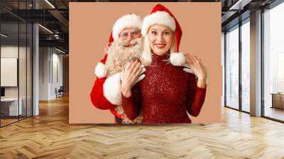 Santa Claus and beautiful mature woman in Christmas hats on brown background Wall mural