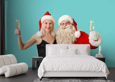 Santa Claus and beautiful mature woman in Christmas hats with glasses of champagne on blue background Wall mural