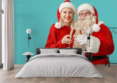 Santa Claus and beautiful mature woman in Christmas hats with glasses of champagne on blue background Wall mural