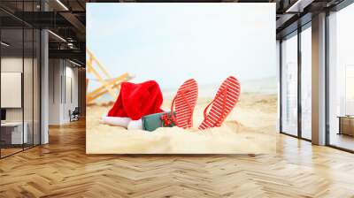 Santa Claus hat with gift box and flip-flops on sea coast. Christmas vacation Wall mural