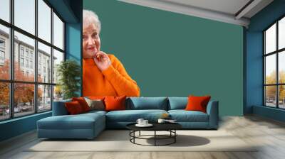 Senior woman in orange sweater on green background with space for text Wall mural