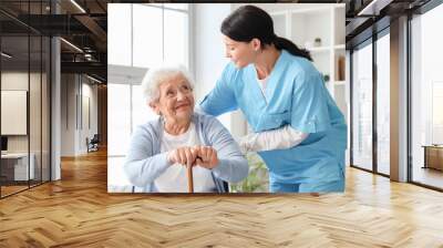 Senior woman in wheelchair with stick and nurse at home Wall mural