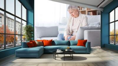 Senior woman suffering from pain in knee at home Wall mural