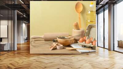 Set of baking utensils with oil and pack of eggs on wooden table near wall Wall mural