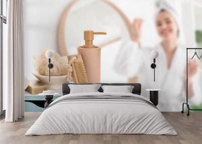 Set of bathing supplies on table in bathroom. Young woman in bathrobe and with cosmetic oil Wall mural