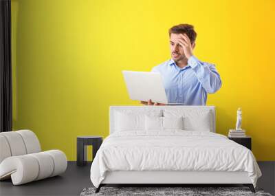 Shocked male programmer with laptop on color background Wall mural