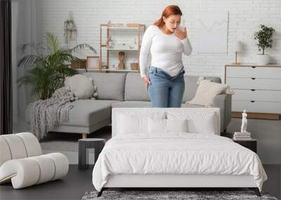 Shocked overweight woman in tight jeans standing on scales at home. Excess weight concept Wall mural