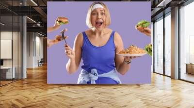 Shocked sporty woman and hands with unhealthy food on lilac background. Overeating concept Wall mural