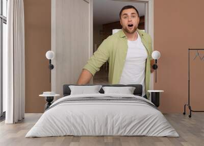 Shocked young man opening wooden door at home Wall mural