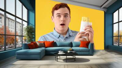 Shocked young man with tasty sandwich wrap on yellow background, closeup Wall mural