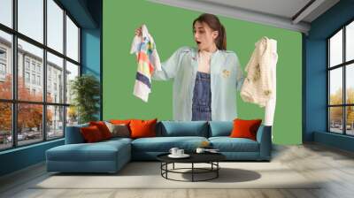 Shocked young woman with dirty laundry on green background Wall mural