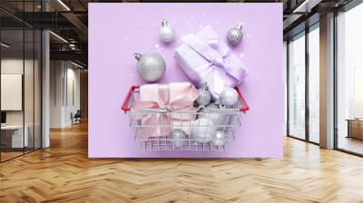 Small shopping basket with Christmas balls and gift boxes on purple background Wall mural