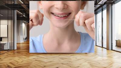 Smiling teenage girl with dental braces holding floss on grey background, closeup Wall mural