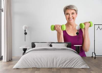 Sporty mature woman with dumbbells on light background Wall mural