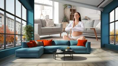 Sporty pregnant woman meditating on mat at home Wall mural