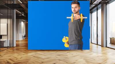 Sporty young man training with dumbbells on color background Wall mural