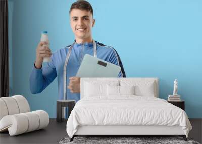 Sporty young man with weight scales and yoghurt on blue background Wall mural