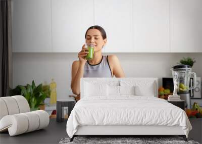 Sporty young woman drinking healthy smoothie in kitchen Wall mural