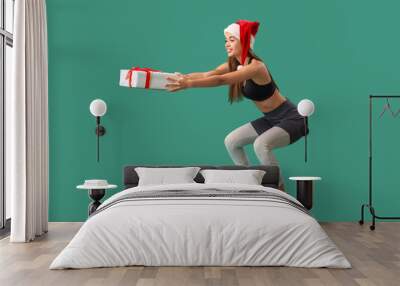 Sporty young woman in Santa hat with Christmas gift training on green background Wall mural