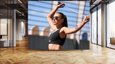 Sporty young woman in sunglasses with skipping rope outdoors Wall mural