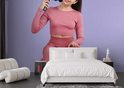 Sporty young woman massaging her neck with percussive massager on fitball against lilac background Wall mural