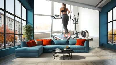 Sporty young woman on treadmill in gym Wall mural