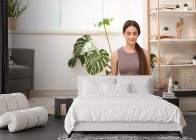 Sporty young woman with bottle of water meditating on fitness mat at home Wall mural