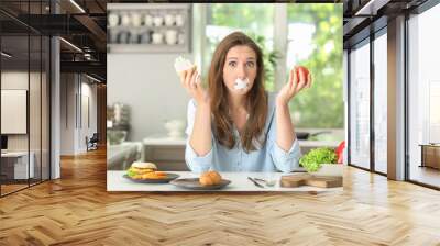 Stressful woman with taped mouth and different products in kitchen. Choice between healthy and unhealthy food Wall mural