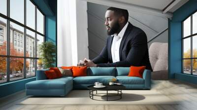 Stylish African-American man sitting in armchair in room Wall mural