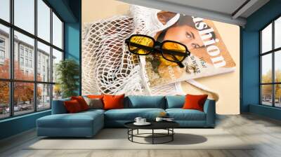 Stylish sunglasses and string bag with magazine on beige background Wall mural