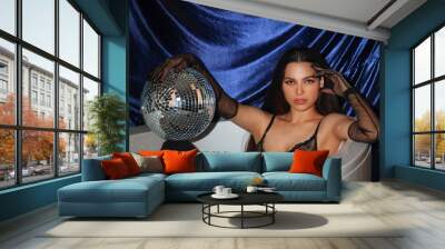 Stylish young woman with disco ball in bathtub against dark blue fabric background Wall mural